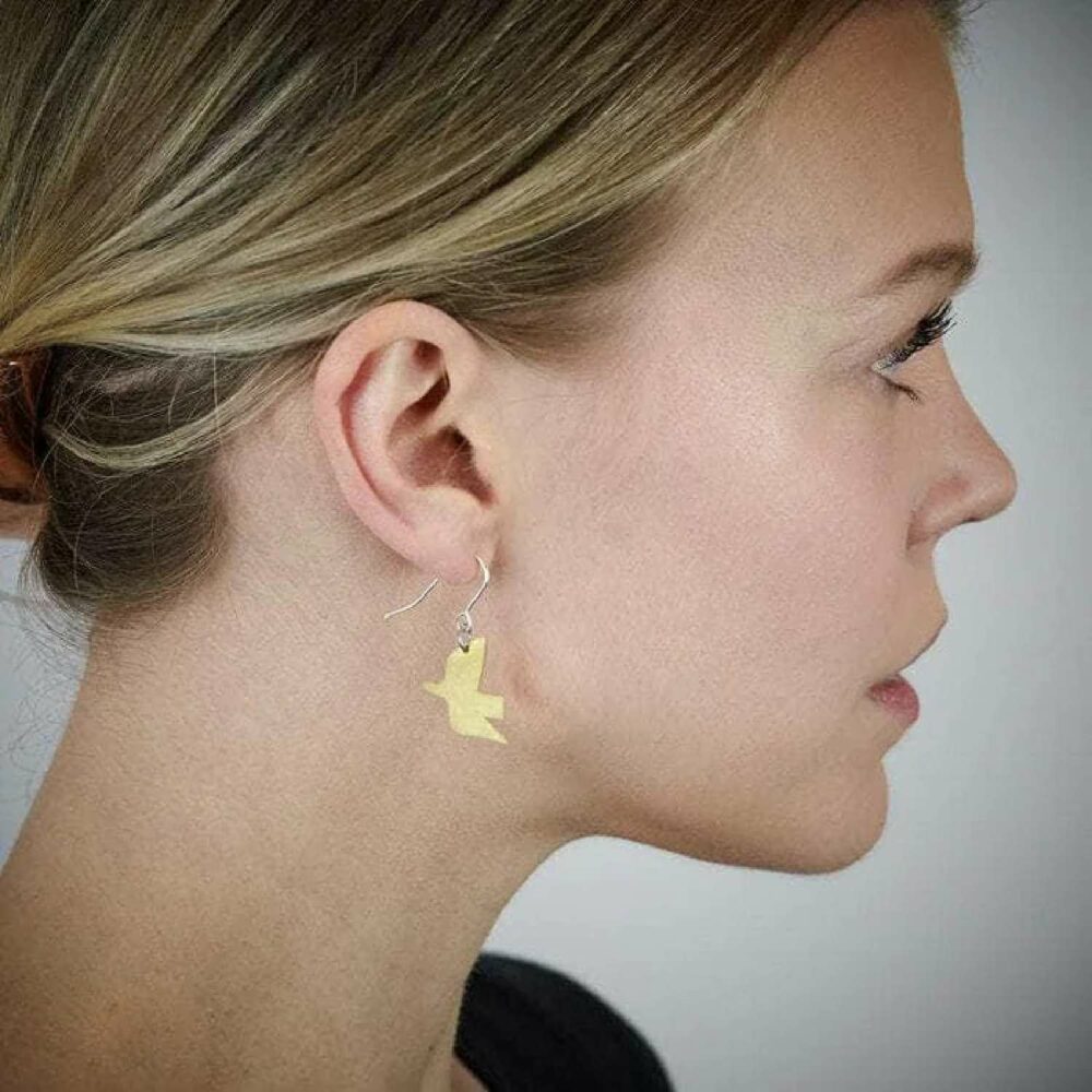 Pivot brass dove earrings shown in model's ear